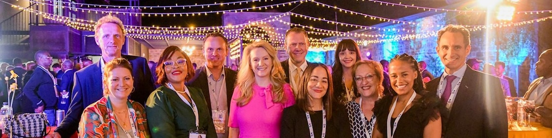 A group of people at an outdoor evening event with string lights above.